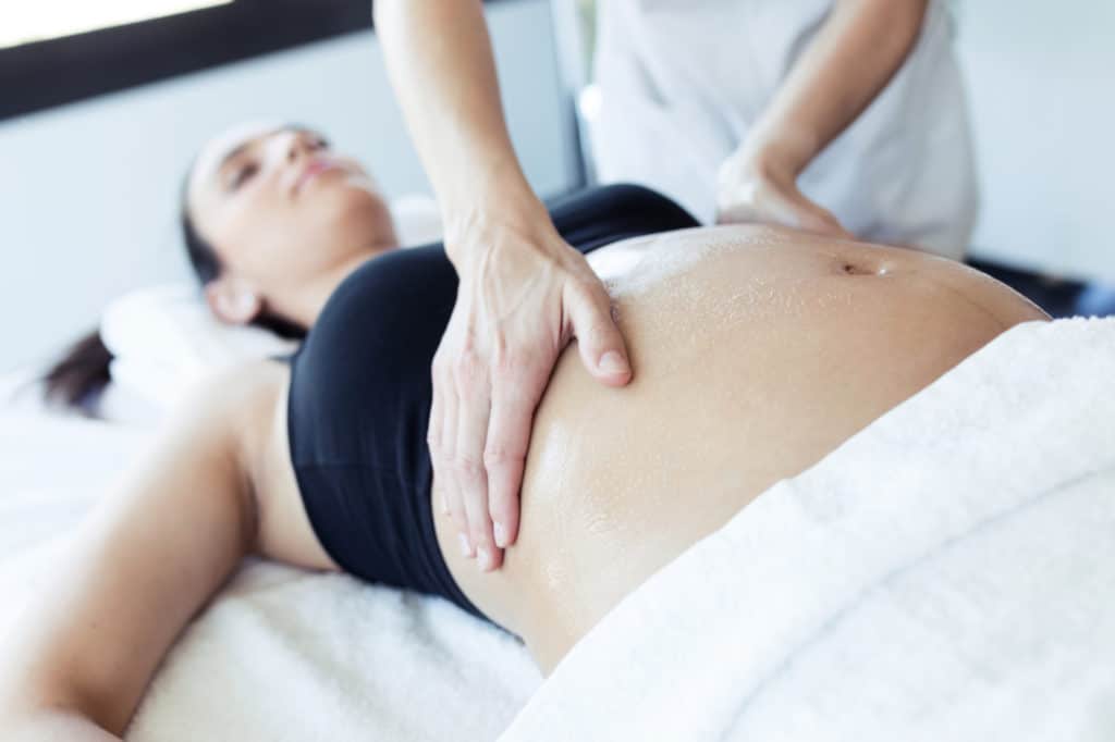 Female physiotherapist massaging tummy on pregnant woman in spa